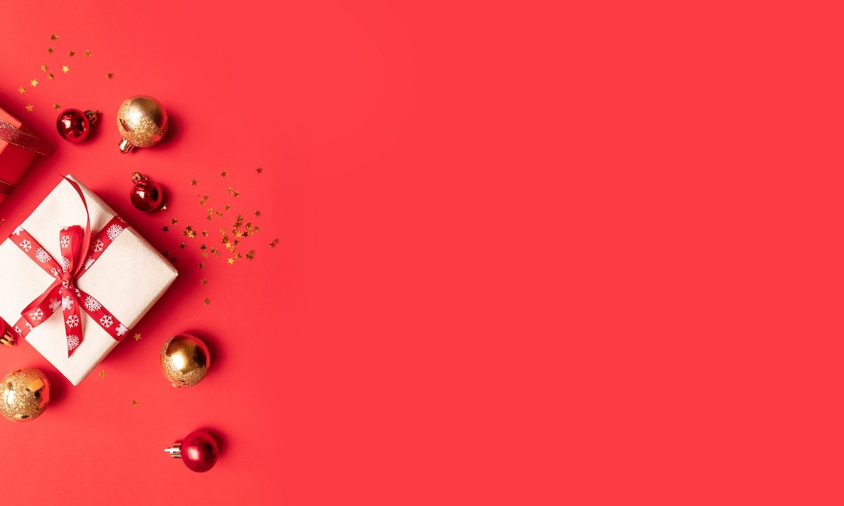 Creative composition with red present box, ribbons, red gold big and small balls, holiday decorations on red background. Flat lay, top view, copy space