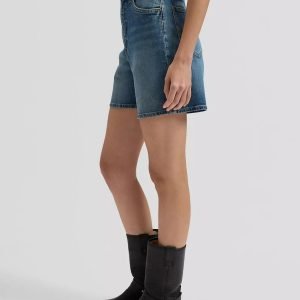 Side view of a person wearing blue denim shorts, a light gray top, and black mid-calf boots.