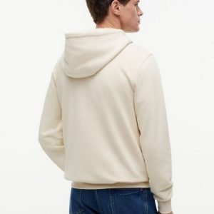 Back view of a man wearing a light beige hoodie and blue jeans against a white background.