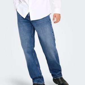 Person wearing a white button-down shirt with blue jeans and black shoes, standing with one hand in a pocket.