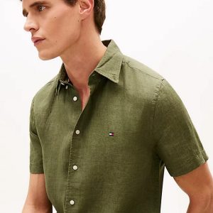 Male model in olive short-sleeve button-down shirt, side profile facing left, neutral background.