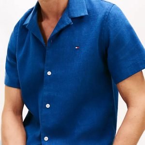 Man wearing a royal blue short-sleeve button-up shirt with a small flag logo on the left chest.
