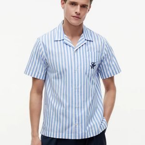 Young man in a blue-and-white vertical stripe short-sleeve shirt with a chest pocket, standing against a light background.