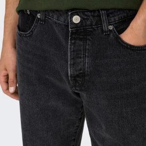 Close-up of black denim jeans at the waist with a metal button; a hand rests in the front pocket, wearing a green shirt.