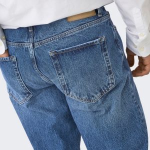 Back view of a person wearing blue denim jeans with a large back pocket and white shirt visible above the waistband, showing stitching details.