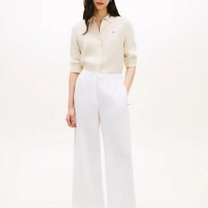 Woman wearing a cream button-down blouse with white wide-leg pants, standing and facing the camera.