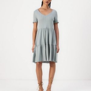 Woman wearing a light blue, short-sleeve, tiered dress with a V-neck, standing against a white background with tan lace-up sandals.