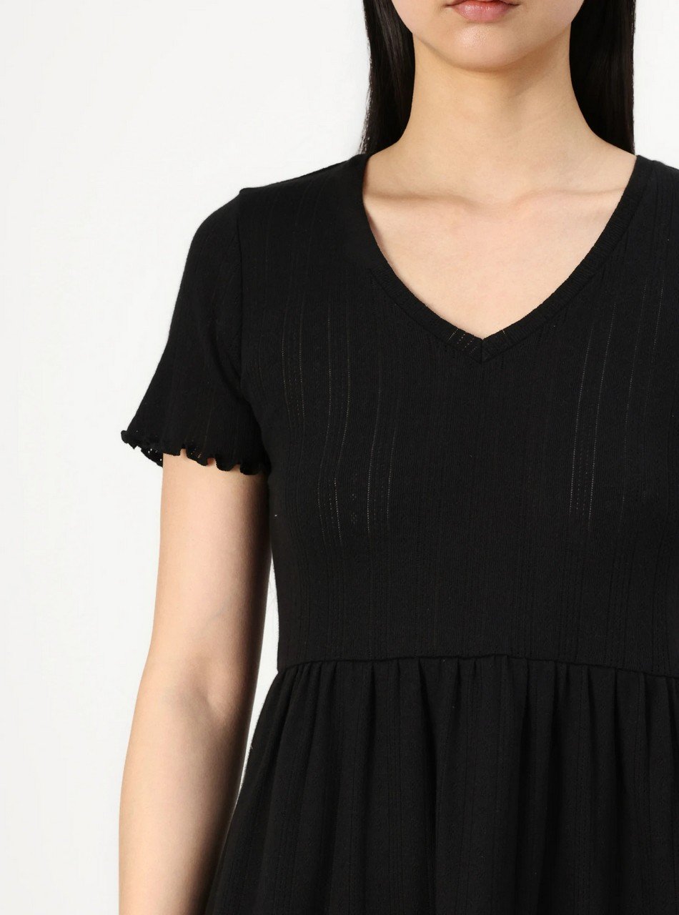 Woman wearing a black short-sleeve V-neck dress with a gathered waist, shown from the chest down against a light background.