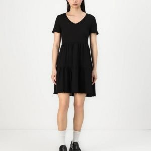 Model wearing a black V-neck short-sleeve tiered dress with white socks and black loafers, standing against a white background.