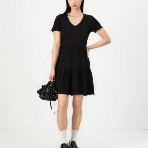 Woman modeling a black V-neck, short-sleeve tiered dress, white socks, black loafers, and a small black floral handbag against a white background.