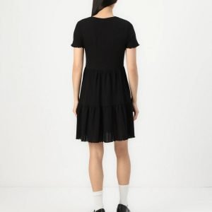 Woman seen from behind wearing a black short-sleeve tiered dress, white socks, and black platform shoes.