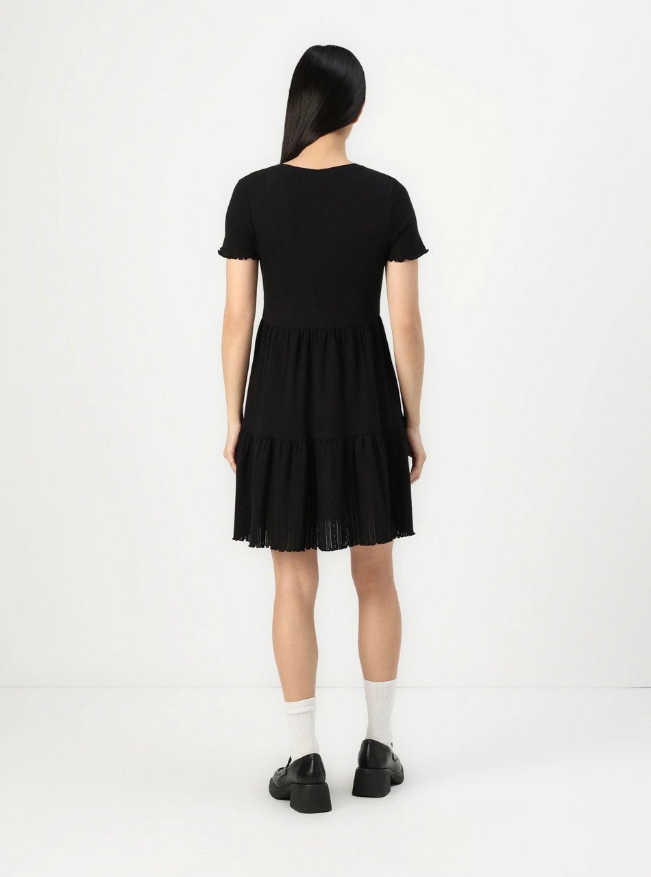 Woman seen from behind wearing a black short-sleeve tiered dress, white socks, and black platform shoes.