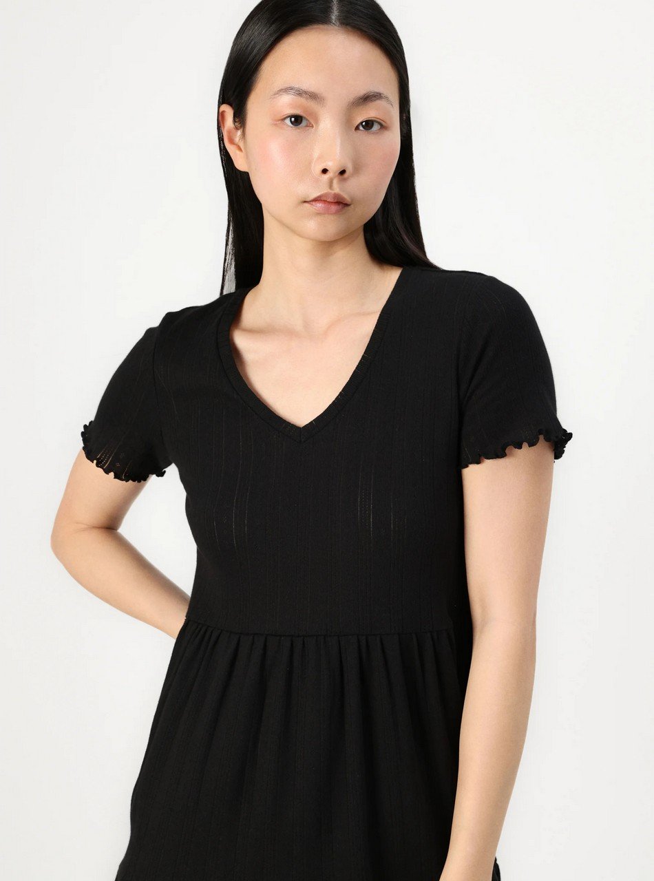 Asian woman wearing a black V-neck dress with short, ruffled sleeves, standing against a white background.