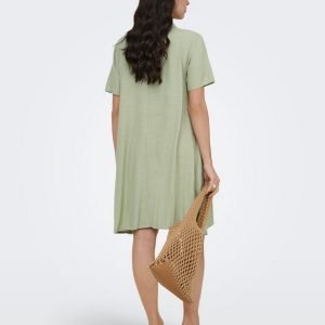 Back view of a woman in a sage green knee-length dress, holding a tan woven tote bag, wearing beige block-heel sandals.