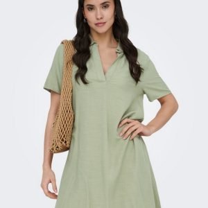 Woman wearing a sage green short-sleeve dress with a woven straw tote over her shoulder.