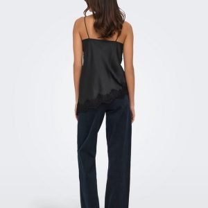 Back view of a woman wearing a black satin camisole with thin straps and lace trim at the hem, paired with dark wide-leg jeans.