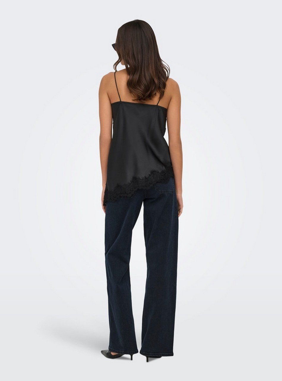 Back view of a woman wearing a black satin camisole with thin straps and lace trim at the hem, paired with dark wide-leg jeans.