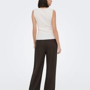 Woman standing with back to camera, wearing a sleeveless white knit top and wide-leg dark brown pants, on a light background.
