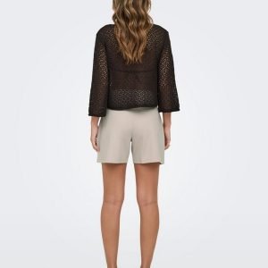 Back view of a woman wearing a black crochet top with three-quarter sleeves and beige shorts, sandals on her feet.