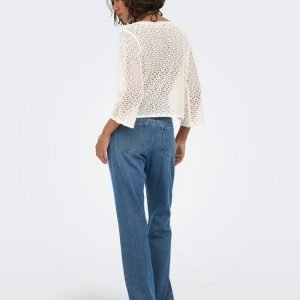 Woman seen from behind wearing a white crochet sweater and high-waisted blue jeans, standing in profile.