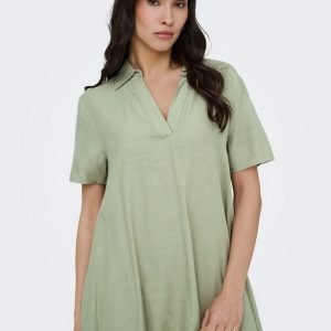 Woman wearing a sage-green, loose-fit short-sleeve dress with a V-neck, holding a woven handbag.