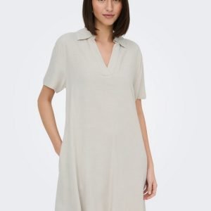 Woman wearing a light beige short-sleeve V-neck dress standing with one hand in her pocket.