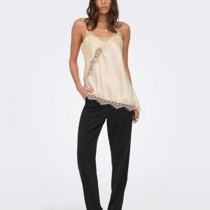 Model wearing an ivory satin camisole with lace trim and black tailored pants, posing against a light background with hands in pockets.