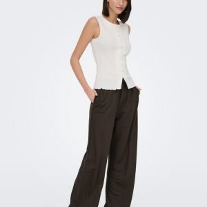 Woman standing in white sleeveless button-front top and wide dark brown trousers, hands in pockets, wearing brown heels.