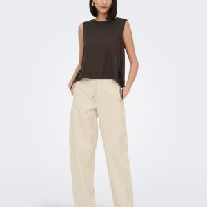 Woman wearing a dark sleeveless top with cream wide-leg pants featuring circular eyelet patterns, hands in pockets.