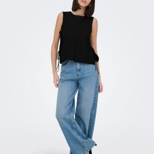 Model wearing a sleeveless black top with side ties and wide-leg blue jeans, standing with one hand in a pocket.