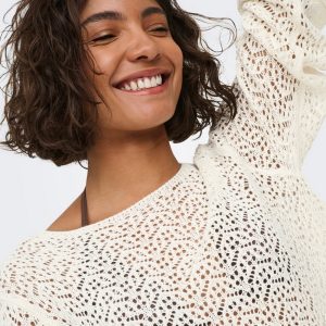 Smiling woman with short curly hair wearing a white crocheted knit sweater.